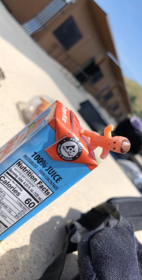 A plastic baby was found sitting on an orange juice box.